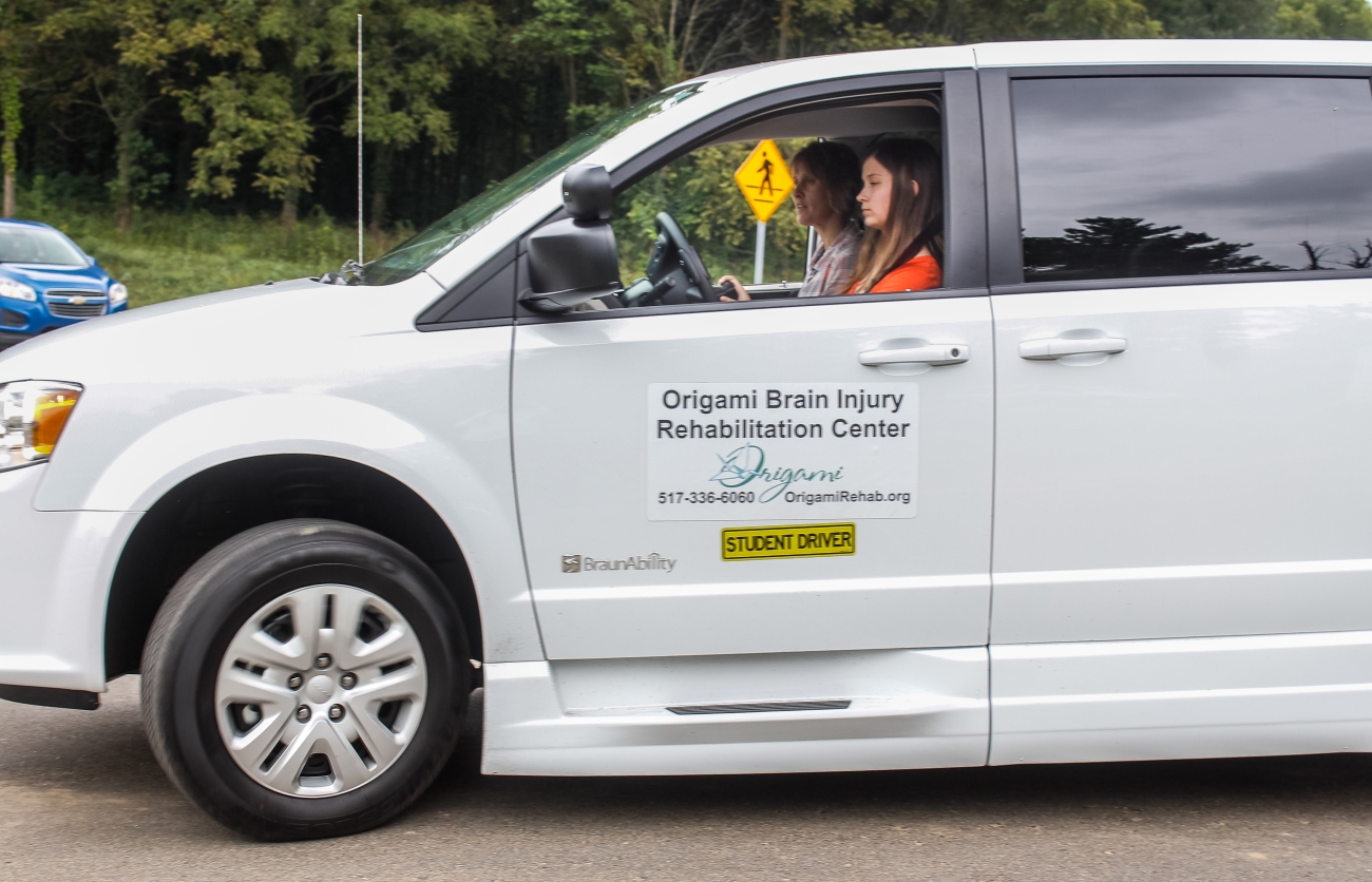 Two women driving in a white van with the Origami logo on it