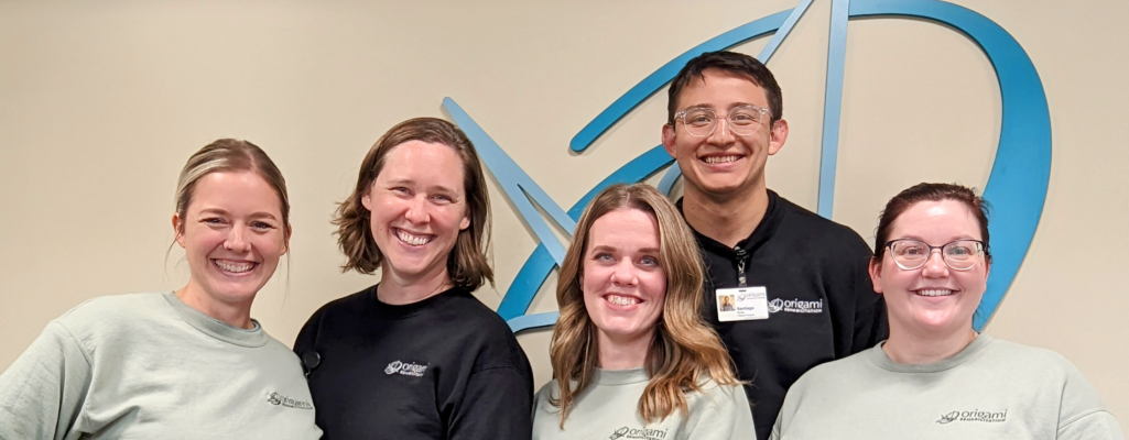Origami Team in front of logo on wall